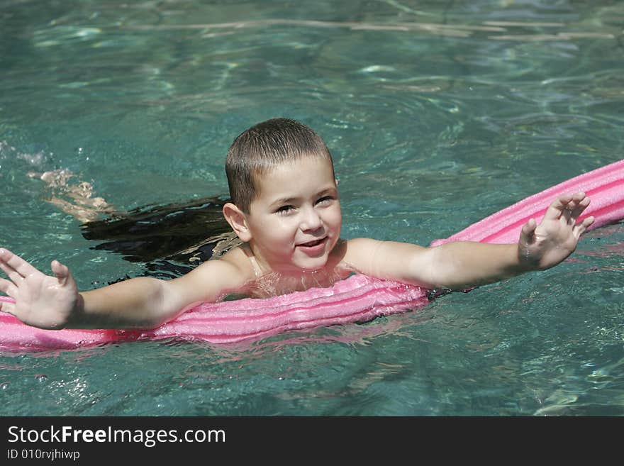 Smiling young boy in crystal clear swimming pool with pink pool toy. Smiling young boy in crystal clear swimming pool with pink pool toy.