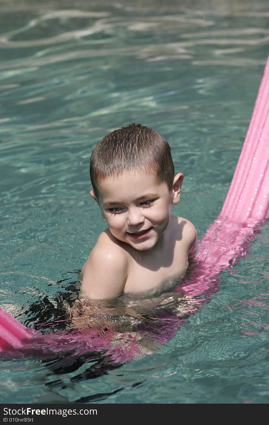 Smiling young boy in crystal clear swimming pool with pink pool toy. . Smiling young boy in crystal clear swimming pool with pink pool toy.