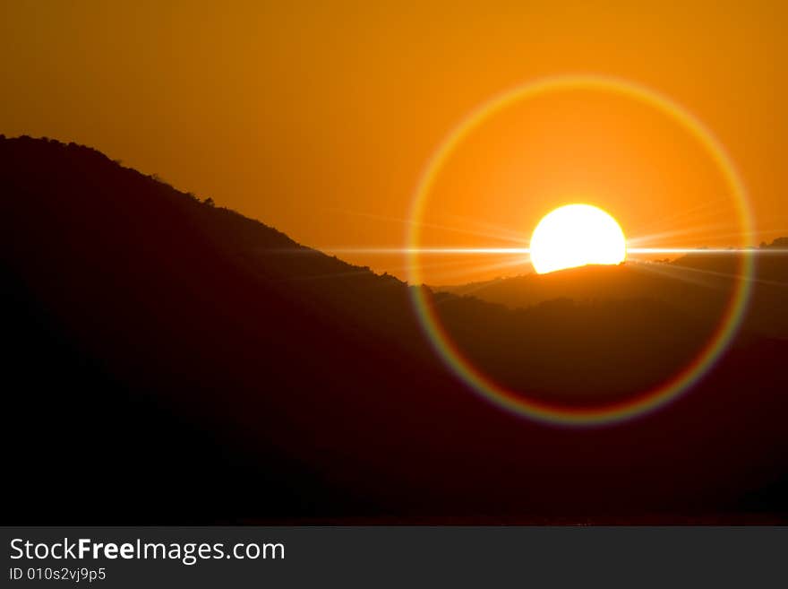 Sunset with halo and sun ray behind mountains