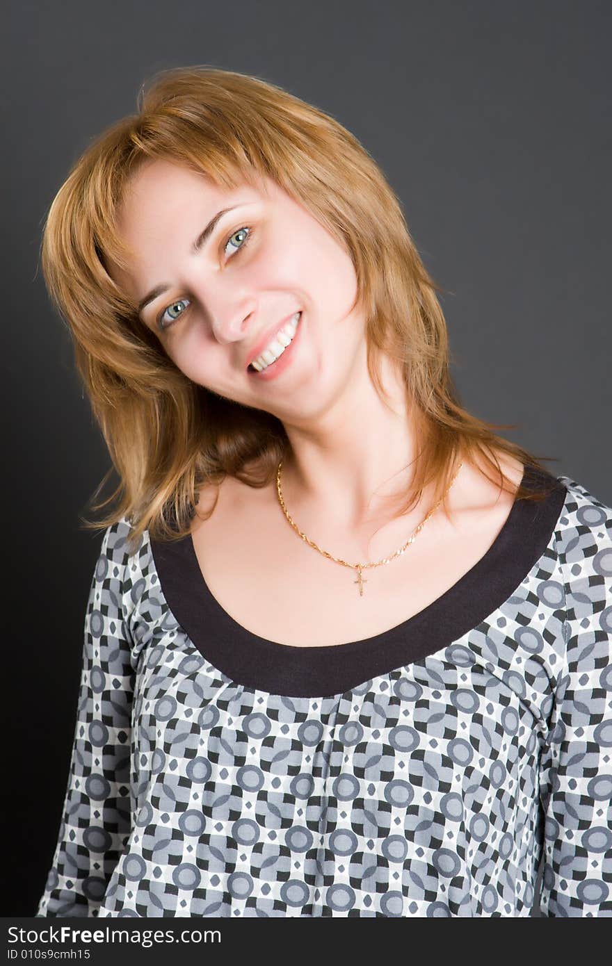 Portrait of the beautiful smiling girl in a grey dress on a dark background. Portrait of the beautiful smiling girl in a grey dress on a dark background