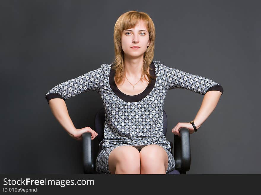 Woman in a grey dress sits on office armchair on a dark background. Woman in a grey dress sits on office armchair on a dark background