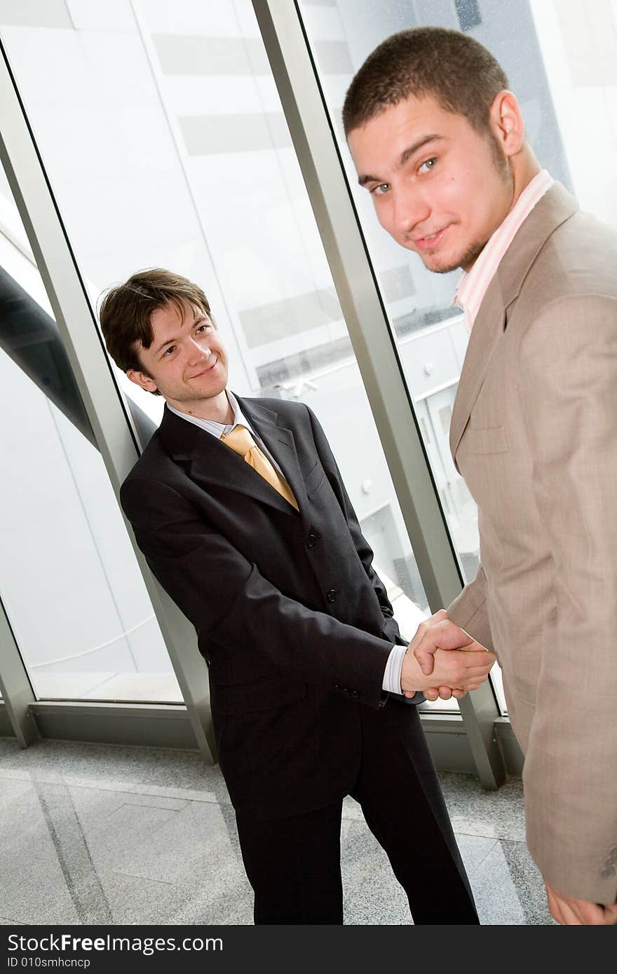 Two young businessmen greet each other by shaking hands. Two young businessmen greet each other by shaking hands