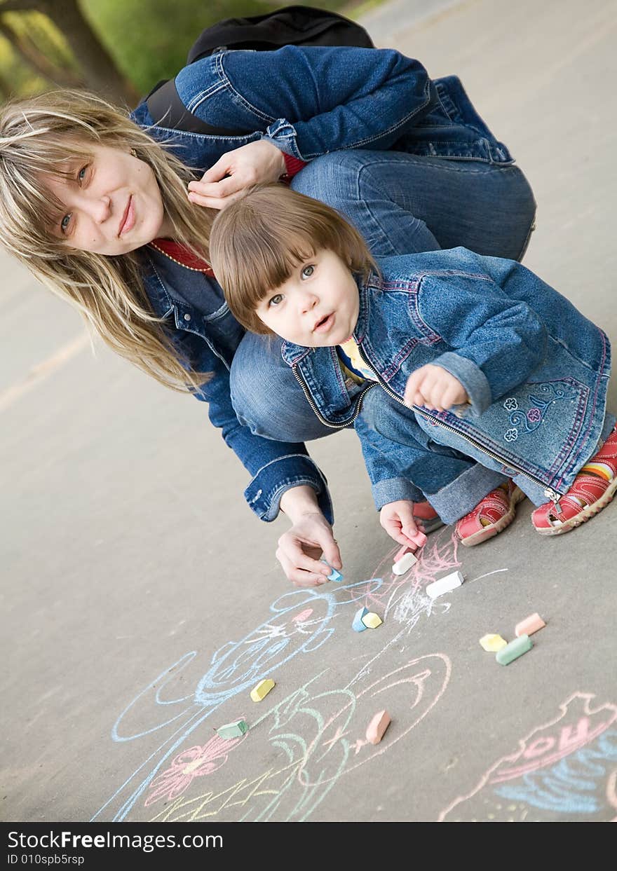 A cute little girl drawing with mom a sketch on a pavement. A cute little girl drawing with mom a sketch on a pavement