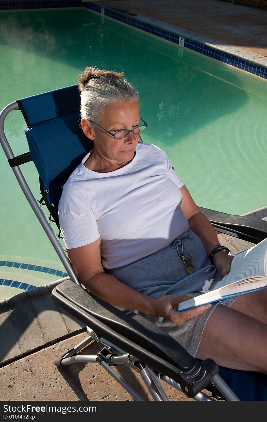 Senior woman sitting by pool reading book