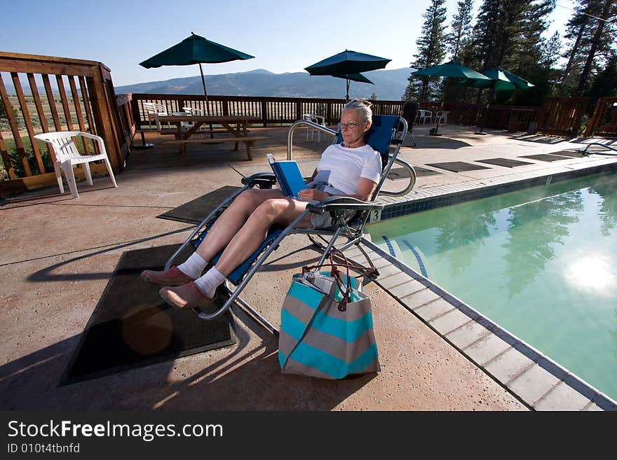 Senior woman sitting by pool reading