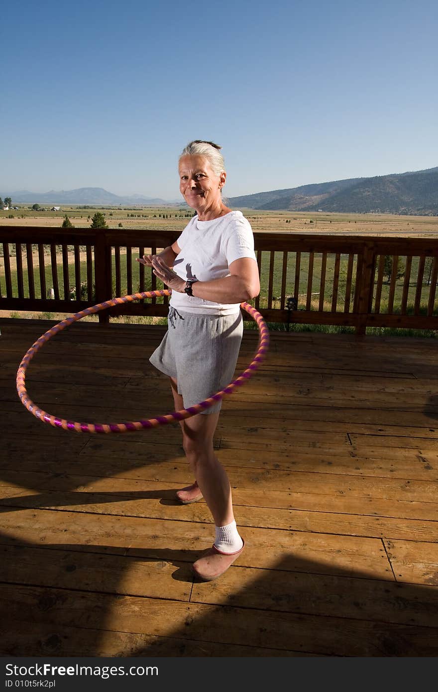 Senior woman hoola hooping on wooden deck with view