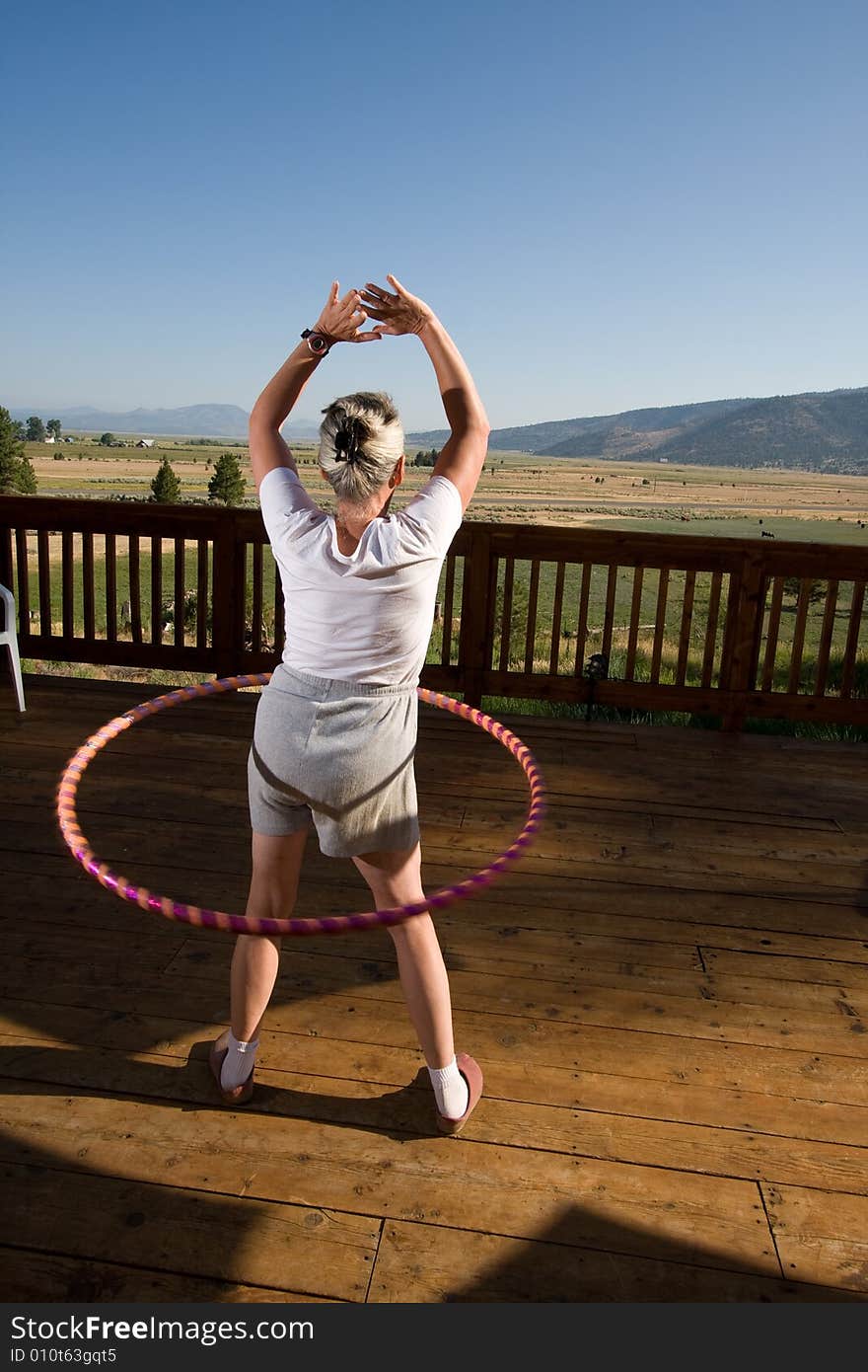 Senior woman hoola hooping on wooden deck with view