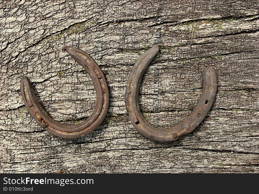 Two metal horseshoes on a piece of seasoned oak. Two metal horseshoes on a piece of seasoned oak.