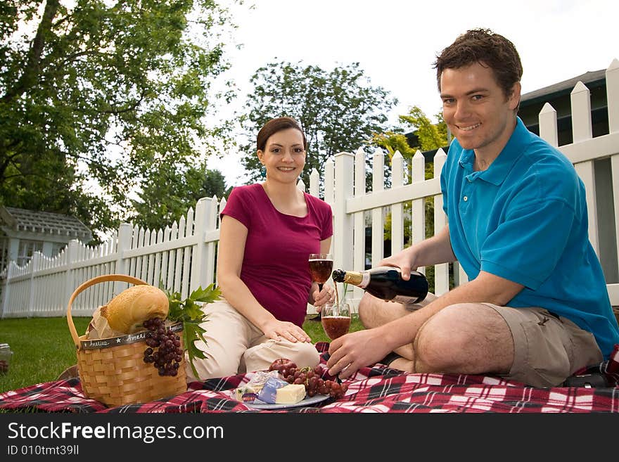 Couple with a picnic spread with wine, cheese and bread.  They are smiling and facing the camera. Horizontally framed shot. Couple with a picnic spread with wine, cheese and bread.  They are smiling and facing the camera. Horizontally framed shot.