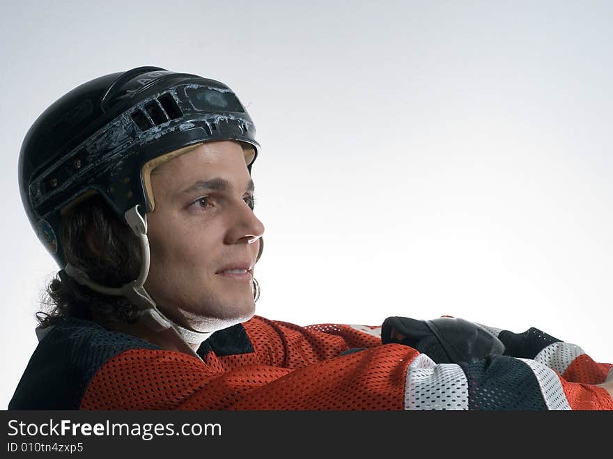 A man, sits down smiling partially, while wearing a full hockey uniform. Horizontally framed shot. A man, sits down smiling partially, while wearing a full hockey uniform. Horizontally framed shot.