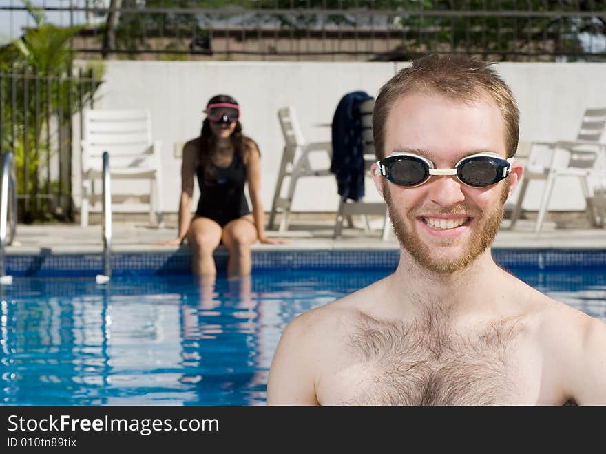 A man and a woman are sitting in a pool.  The woman is on the far end of the pool looking at the camera.  The man is standing right in front of the camera looking at it.  Horizontally framed photo. A man and a woman are sitting in a pool.  The woman is on the far end of the pool looking at the camera.  The man is standing right in front of the camera looking at it.  Horizontally framed photo.