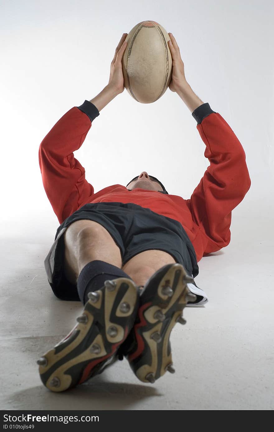 Man relaxing on the floor holding a football above his head. Vertically framed photograph. Man relaxing on the floor holding a football above his head. Vertically framed photograph