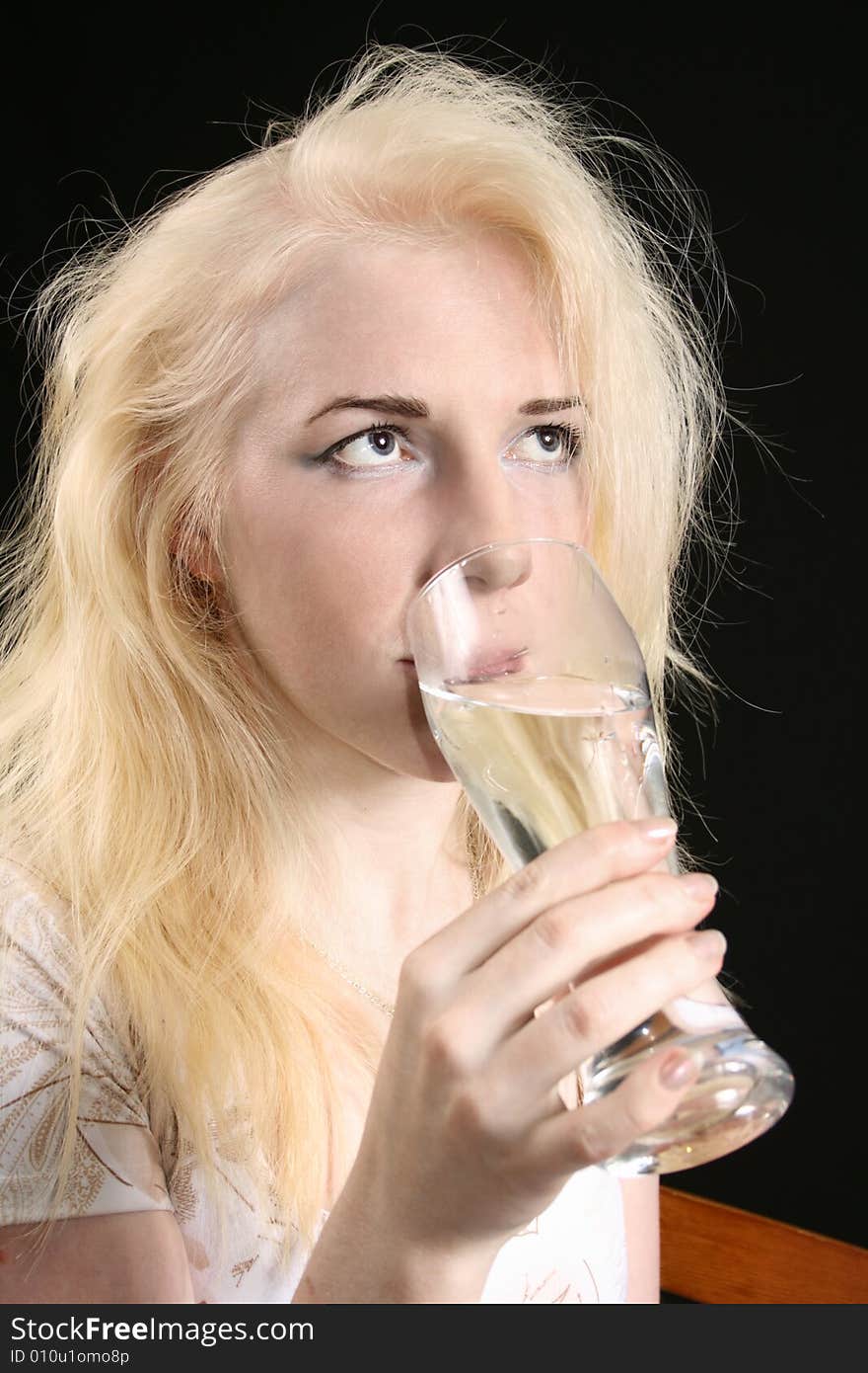 Young blond woman holds glass against the black background. Young blond woman holds glass against the black background.