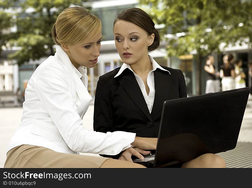 Two attractive businesswomen working on laptop outdoors. Two attractive businesswomen working on laptop outdoors