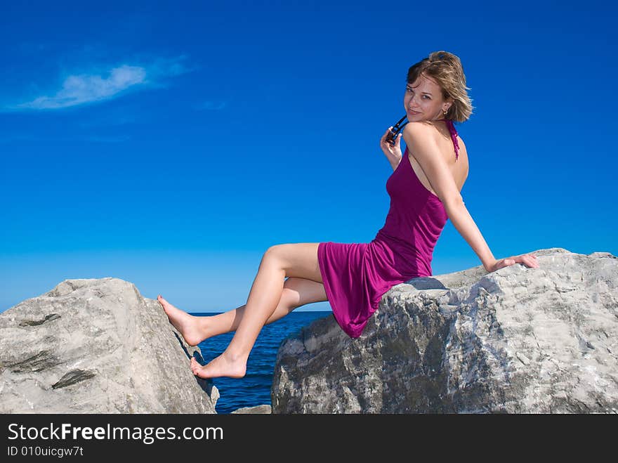 Young lady sitting on the rock in the blue sky. Young lady sitting on the rock in the blue sky