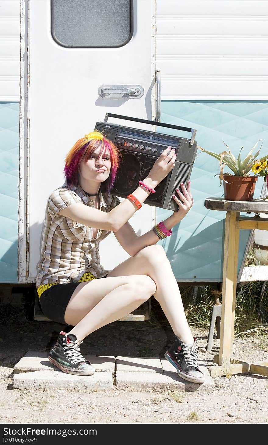 Punk girl with brightly colored hair sitting on trailer step holding boom box. Punk girl with brightly colored hair sitting on trailer step holding boom box