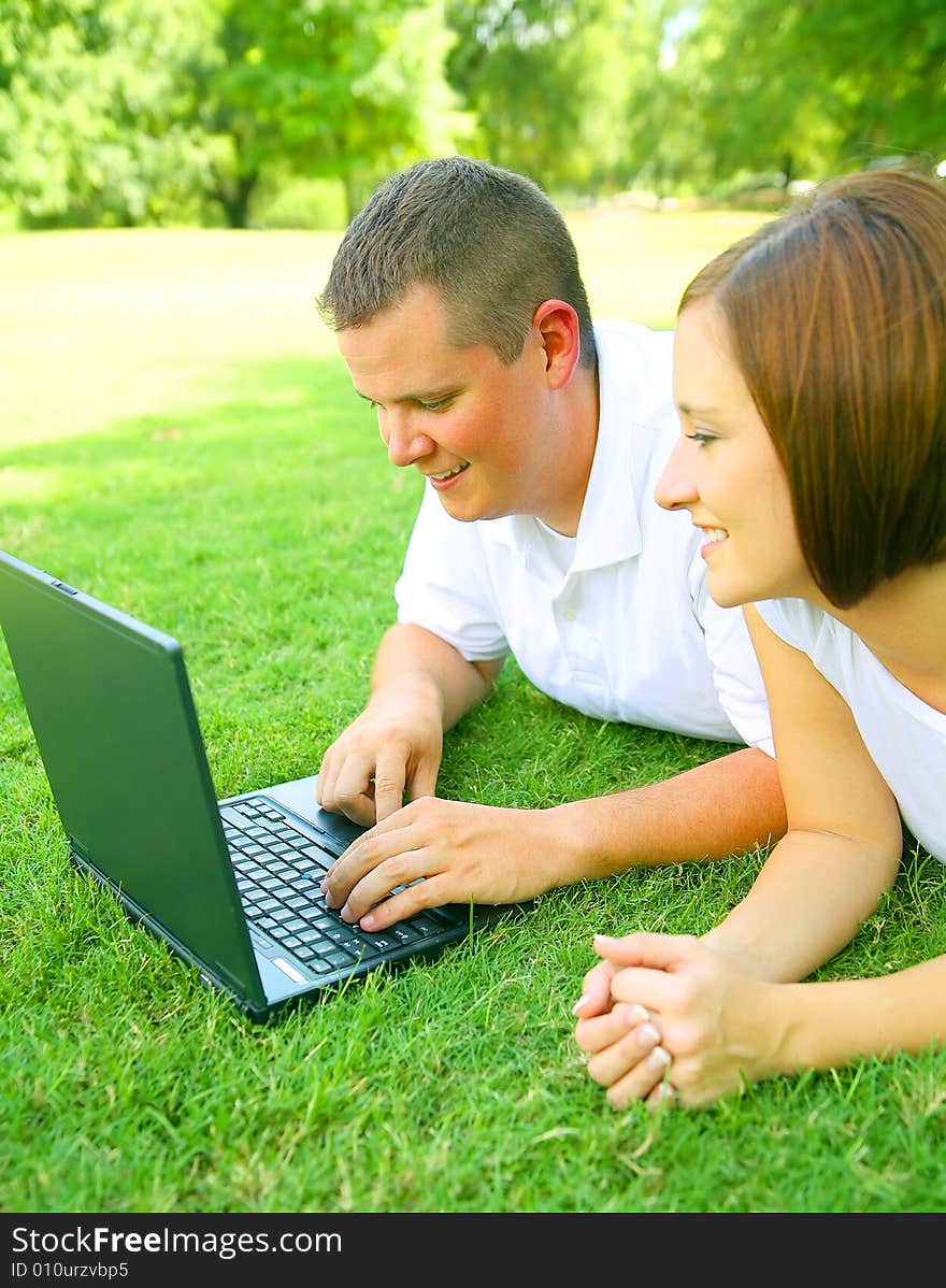 Caucasian couple using or working with computer outdoor on the grass. Caucasian couple using or working with computer outdoor on the grass