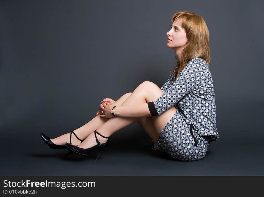 Young nice girl in a beautiful grey dress sits on a dark background. Young nice girl in a beautiful grey dress sits on a dark background