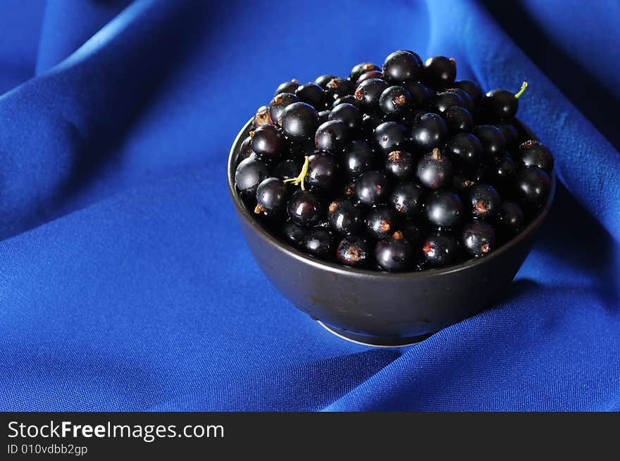 Black currants in the black bowl on the blue background. Narrow depth of field. Black currants in the black bowl on the blue background. Narrow depth of field.