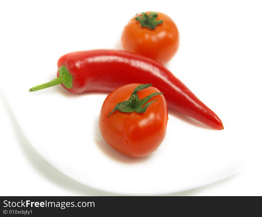 Two fresh tomatoes and a ripe chili pepper on a white plate and isolated on white background. Two fresh tomatoes and a ripe chili pepper on a white plate and isolated on white background