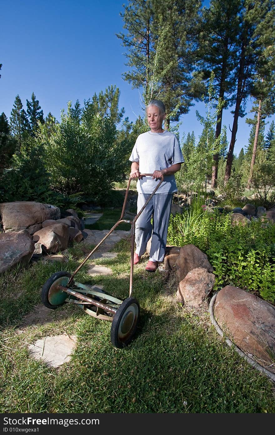 Attractive senior woman mowing lawn with hand mower