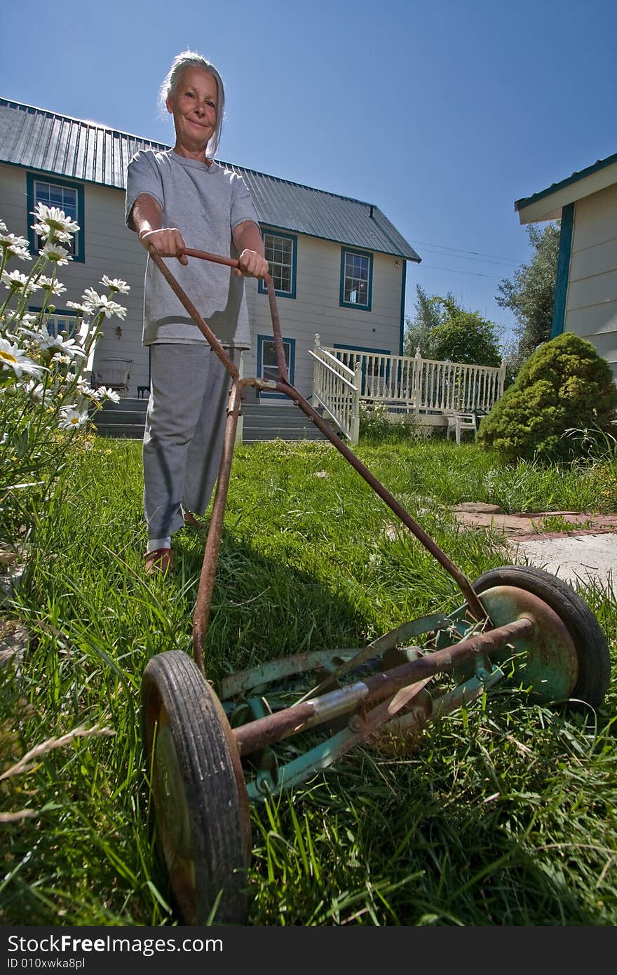 Attractive senior woman mowing lawn with hand mower