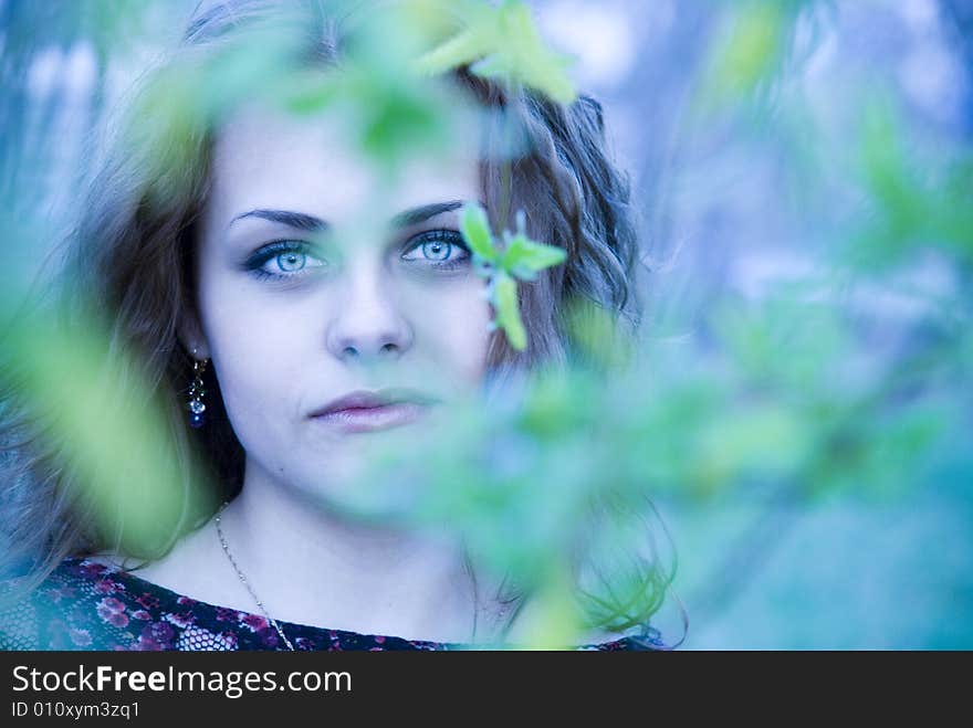 Portrait of girl with a curly red hair, which looks charming through green leaves on a foreground. Portrait of girl with a curly red hair, which looks charming through green leaves on a foreground