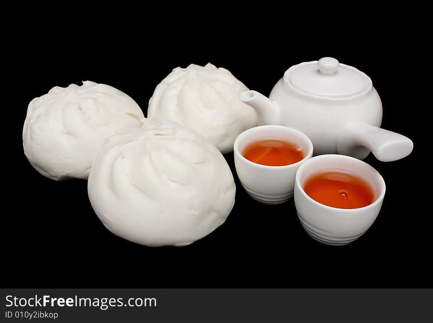 Chinese barbecued pork bun with teapot and teacups on black background.