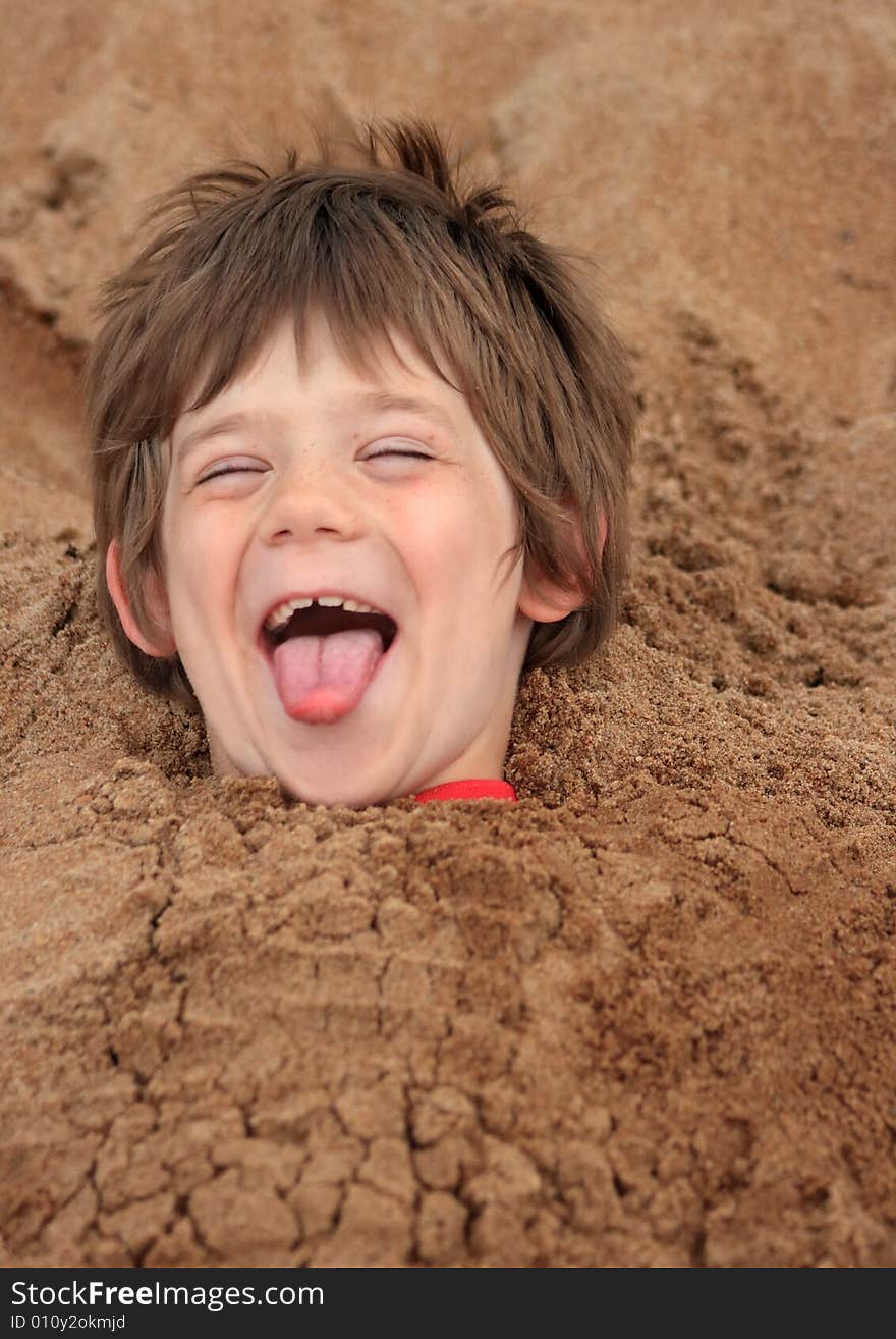 A happy young boy buried in sand at a playground. A happy young boy buried in sand at a playground