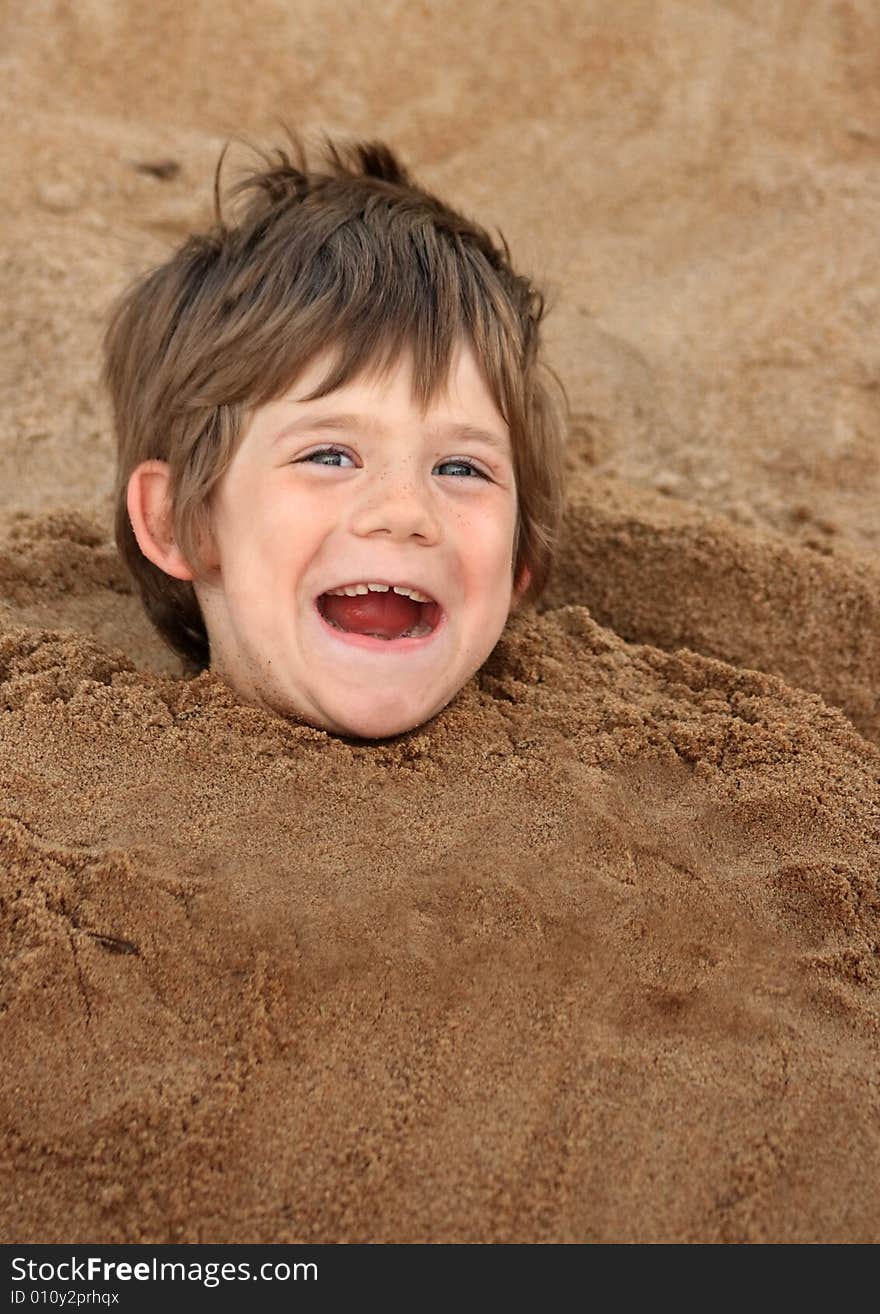 A happy young boy buried in sand at a playground. A happy young boy buried in sand at a playground