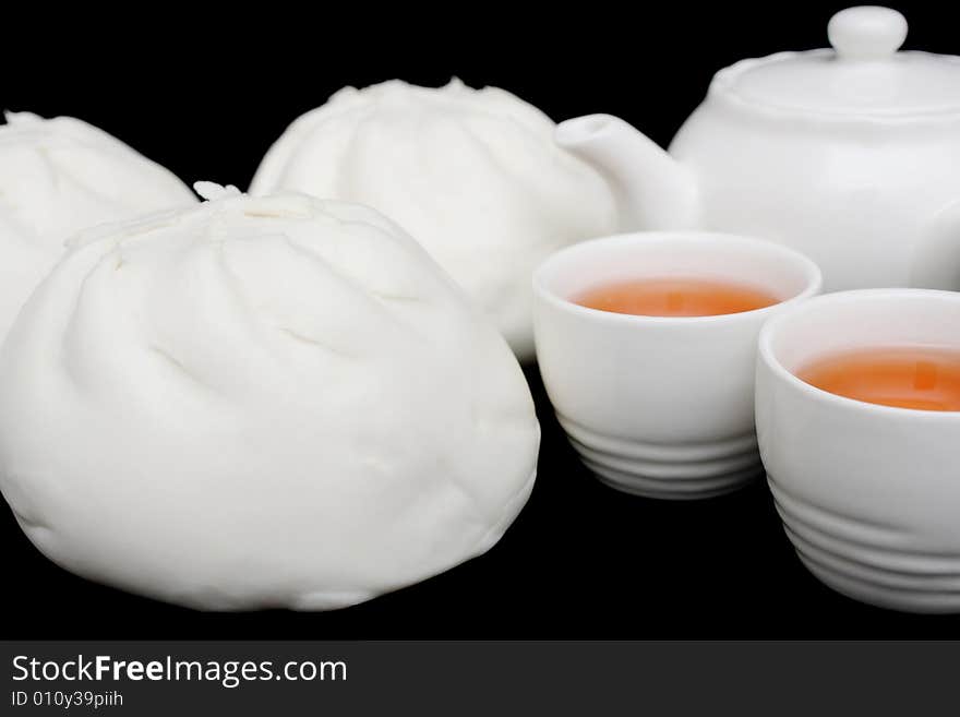 Chinese barbecued pork bun with teapot and teacups on black background.