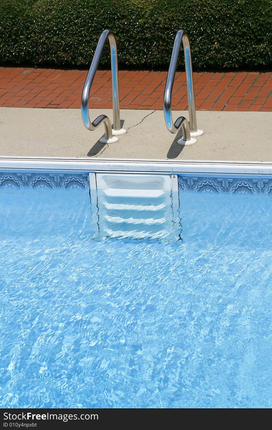 A view of white steps or ladder and metal railing going into an empty swimming pool. A view of white steps or ladder and metal railing going into an empty swimming pool.