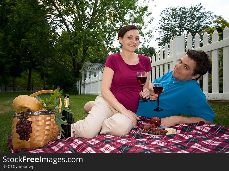 A couple on a picnic holding wine glasses. They are sitting very close to one another and are both smiling directly at the camera. Horizontally framed shot. A couple on a picnic holding wine glasses. They are sitting very close to one another and are both smiling directly at the camera. Horizontally framed shot.