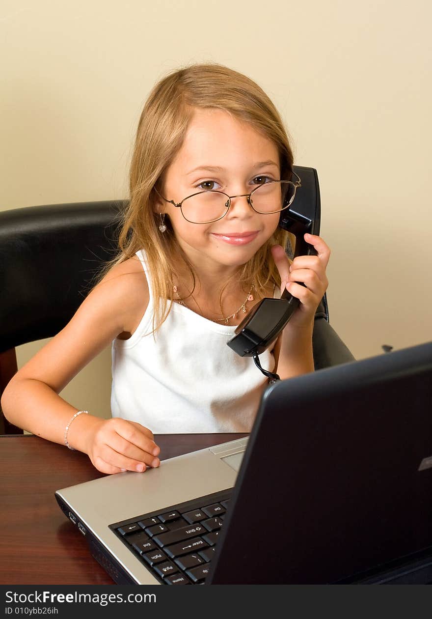 A young girl about 6 pretends to be busy at her notebook computer while wearing glasses too big for her head. A young girl about 6 pretends to be busy at her notebook computer while wearing glasses too big for her head.