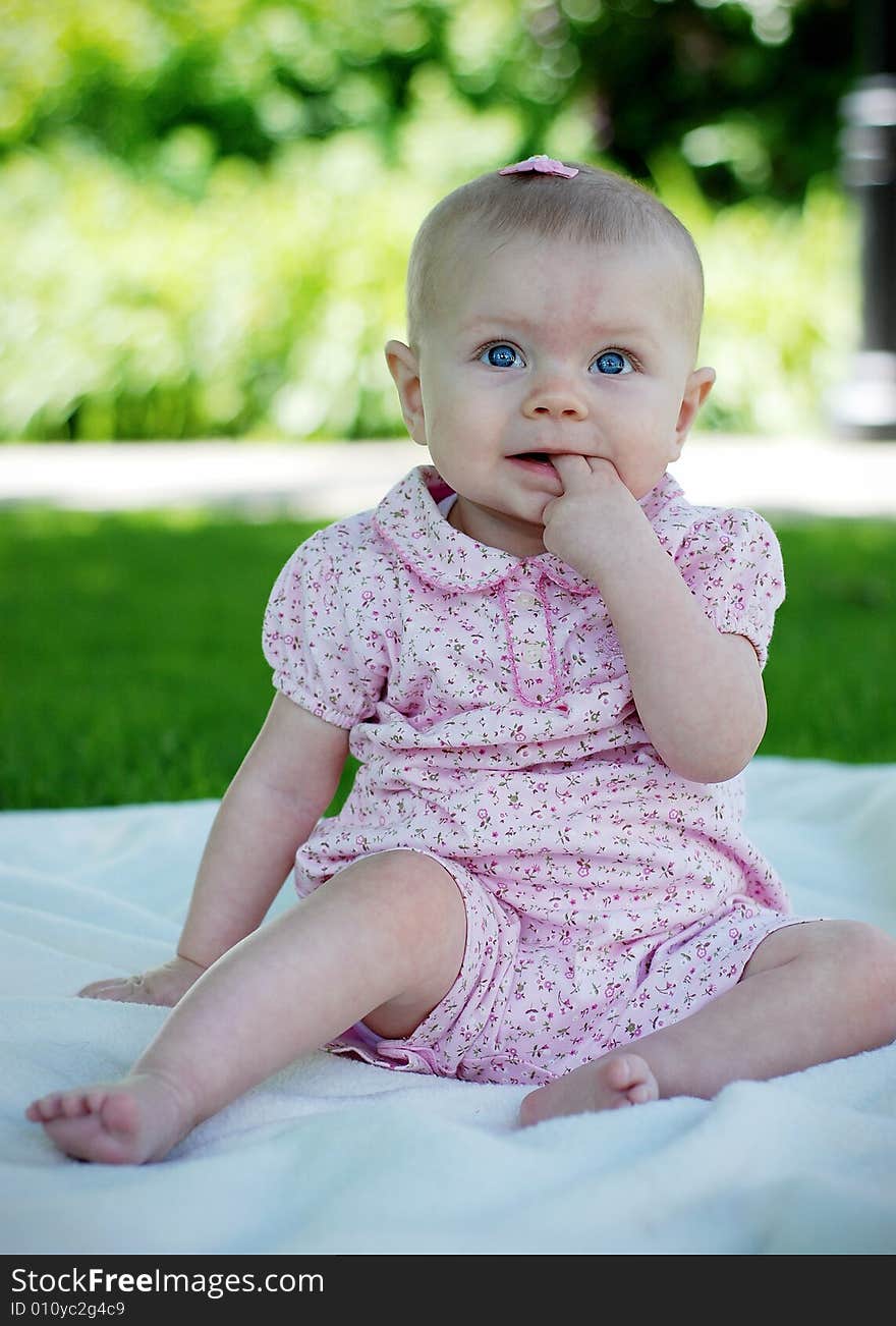 A young baby, bites her index finger, while sitting and wearing a pink outfit and bow. Vertically framed shot. A young baby, bites her index finger, while sitting and wearing a pink outfit and bow. Vertically framed shot.