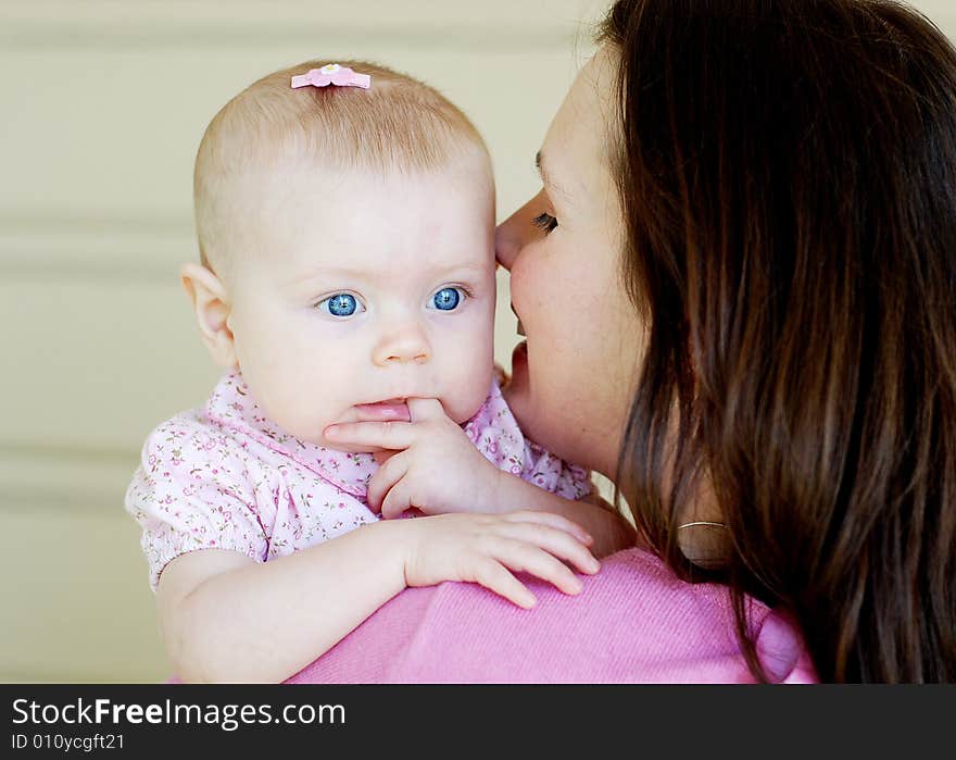 A mother, looks at her baby, and smiles. The baby looks back behind her moms shoulder, sticking her finger in her mouth. Horizontally framed shot. A mother, looks at her baby, and smiles. The baby looks back behind her moms shoulder, sticking her finger in her mouth. Horizontally framed shot.