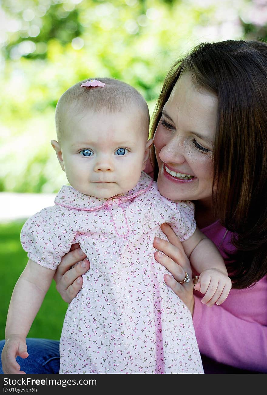 A mother and baby, both dressed in pink. The mother, playing with her child and the baby smiling at the camera. Vertically framed shot. A mother and baby, both dressed in pink. The mother, playing with her child and the baby smiling at the camera. Vertically framed shot.