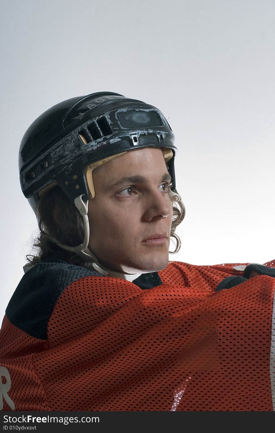 A young man, wearing a full hockey uniform, sits on the floor, looking serious. Vertically framed shot. A young man, wearing a full hockey uniform, sits on the floor, looking serious. Vertically framed shot.