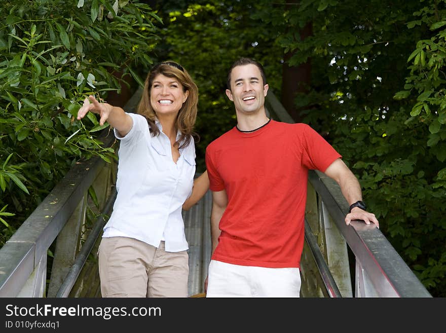 Happy couple standing on a bridge smiling and pointing. Horizontally framed photograph. Happy couple standing on a bridge smiling and pointing. Horizontally framed photograph