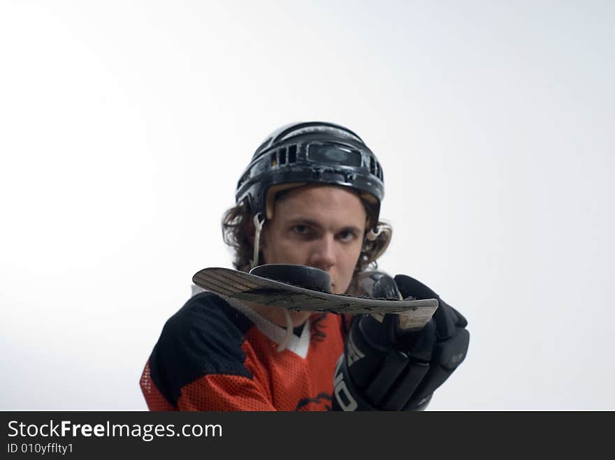 A man stands looking serious, wearing a hockey uniform. He holds out his hockey stick, balancing a puck. Horizontally framed shot. A man stands looking serious, wearing a hockey uniform. He holds out his hockey stick, balancing a puck. Horizontally framed shot.