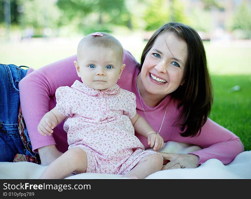 A mother and her baby, sit and lie down in a patch of grass, smiling. Horizontally framed shot. A mother and her baby, sit and lie down in a patch of grass, smiling. Horizontally framed shot.