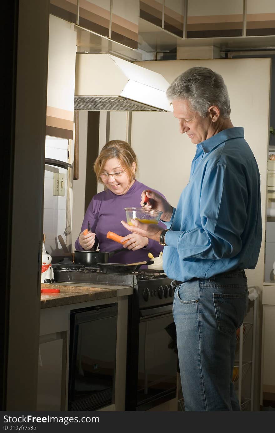 A couple cooking together in a kitchen setting.  They are smiling and enjoying one another. Vertically framed shot. A couple cooking together in a kitchen setting.  They are smiling and enjoying one another. Vertically framed shot.