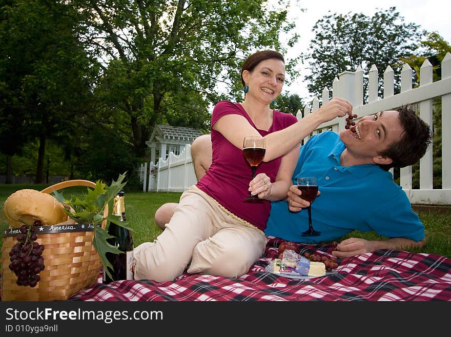 A couple toasting wine glasses on a picnic spread.  They are joking with each other and she is feeding him grapes. Horizontally framed shot. A couple toasting wine glasses on a picnic spread.  They are joking with each other and she is feeding him grapes. Horizontally framed shot.