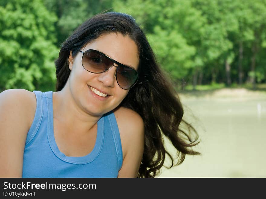 A beautiful girl, wearing sunglasses, sitting on a bench near a lake, smiling. A beautiful girl, wearing sunglasses, sitting on a bench near a lake, smiling