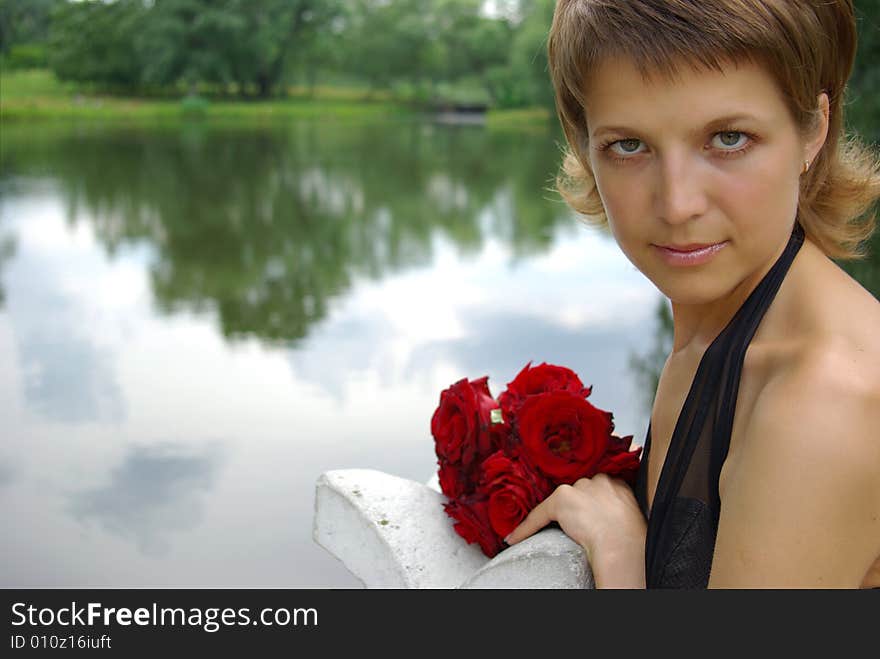 Attractive young woman with red flowers against lake reflection