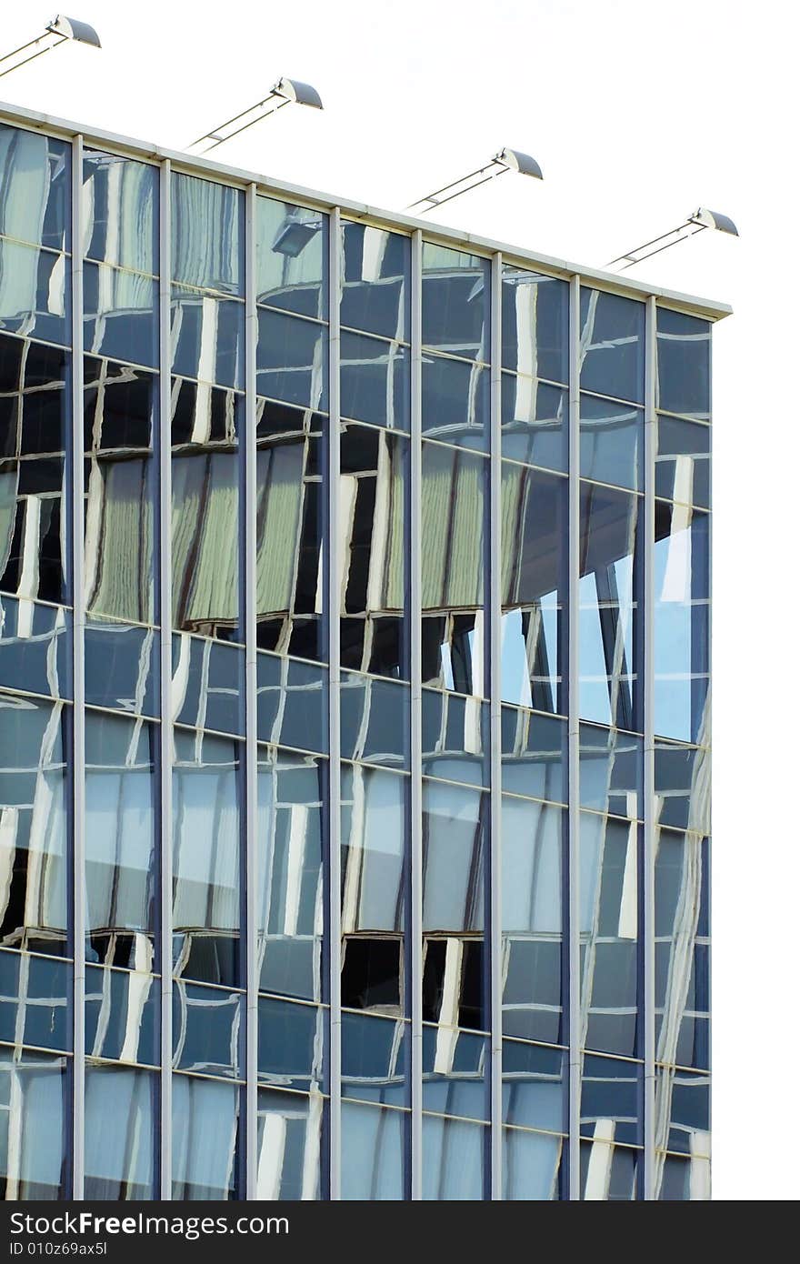 A photo of a wall of an offise building with a number windows and reflections of a near building in it. A photo of a wall of an offise building with a number windows and reflections of a near building in it