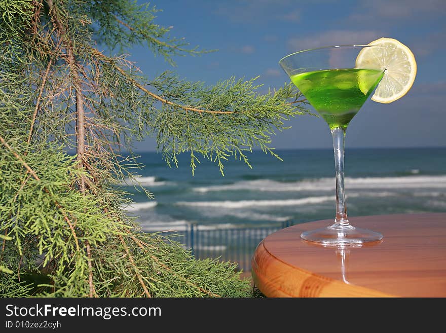 Tropical drink with the lobule of lemon in beautiful glass stands on a wooden table ashore exterminating. Tropical drink with the lobule of lemon in beautiful glass stands on a wooden table ashore exterminating