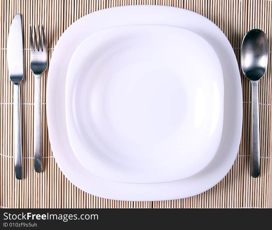 A white plate with cutlery on bamboo