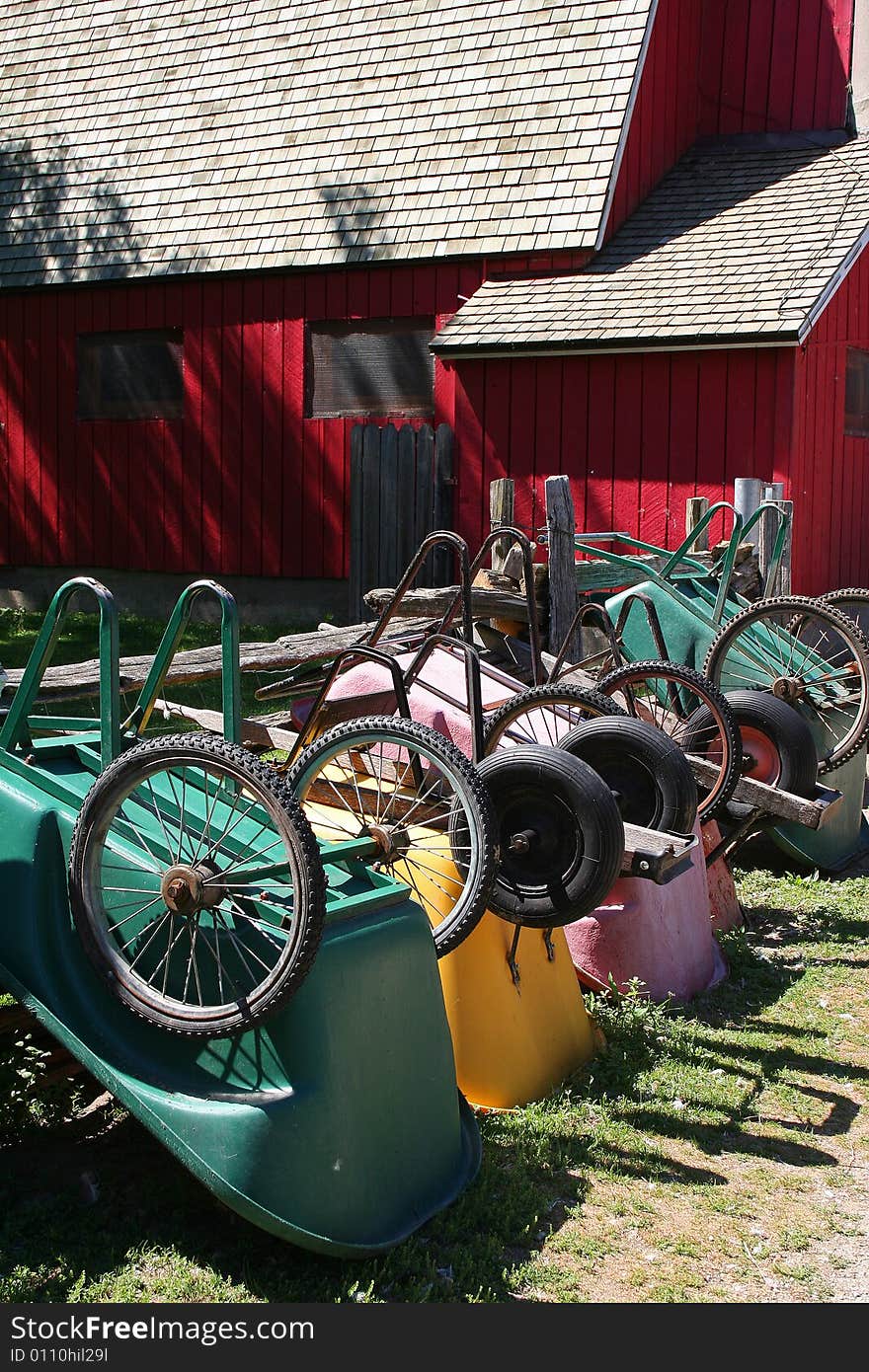 Colourful wheelbarrows lined up against a fence in front of a red barn