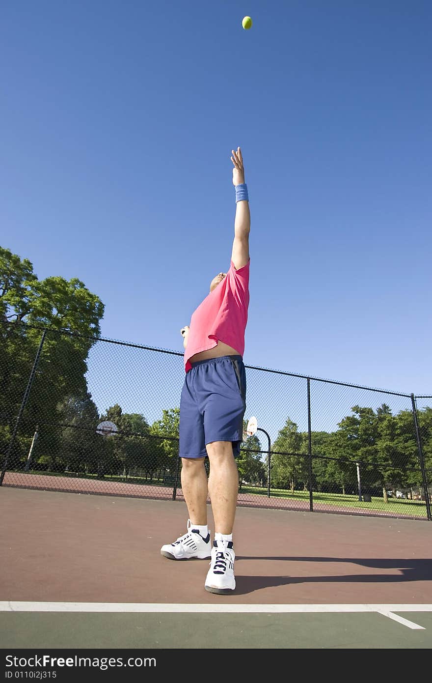 A man is outside on a tennis court playing tennis.  He is reaching up to hit the ball and looking at his racket. A man is outside on a tennis court playing tennis.  He is reaching up to hit the ball and looking at his racket.